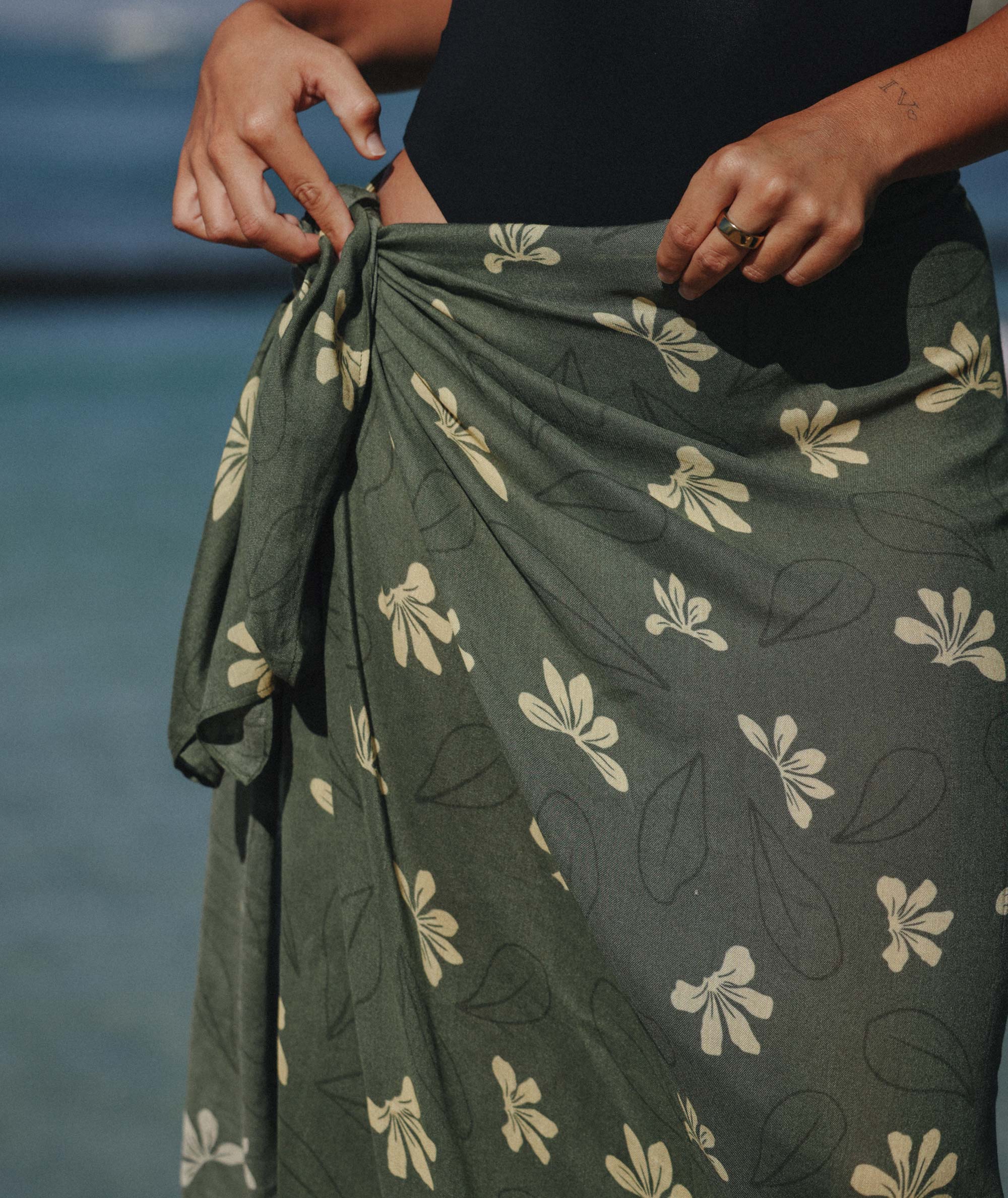 Person wearing a green floral-patterned skirt with a blurred natural background