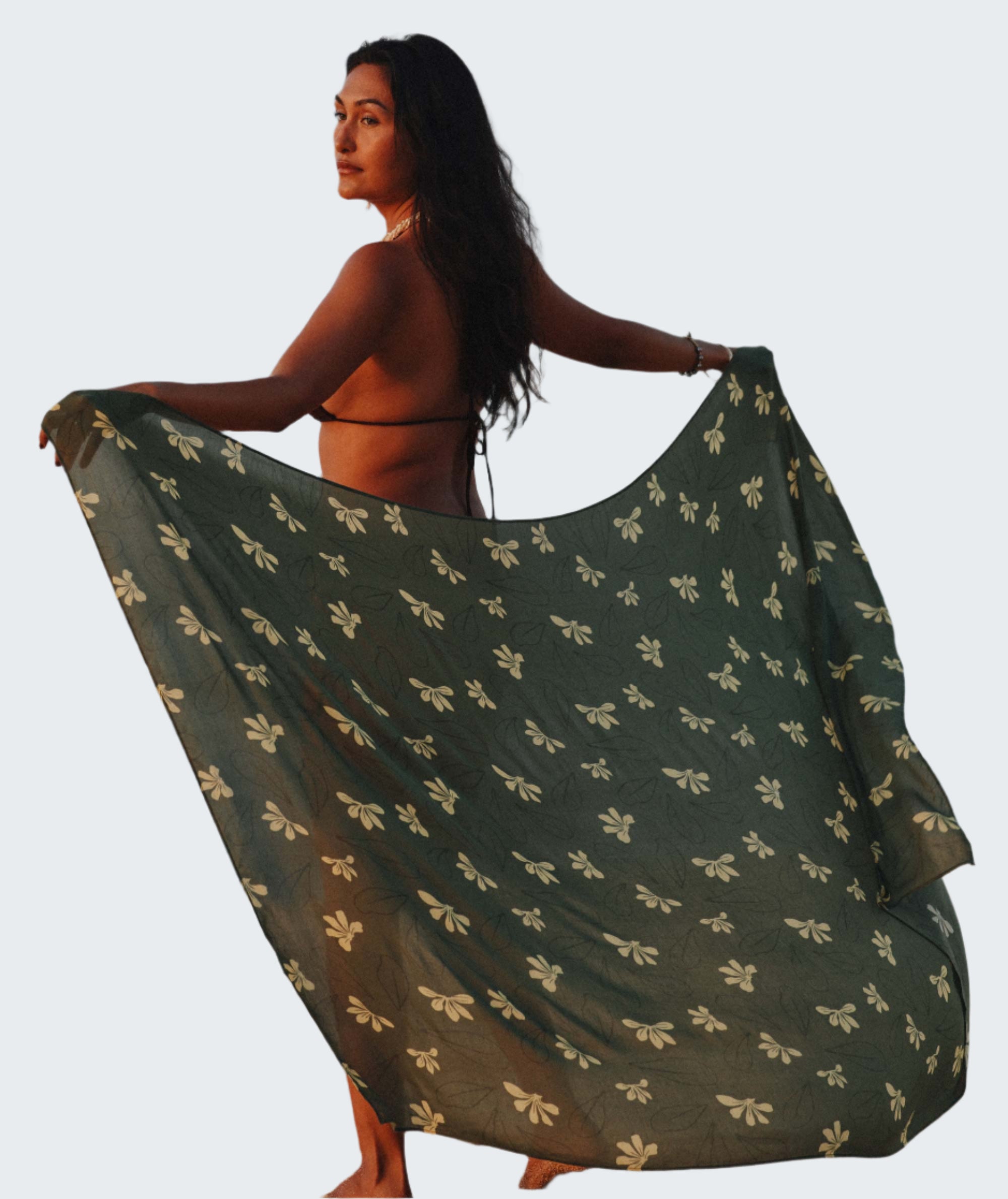 Woman holding a green patterned scarf on a beach with ocean and sky in the background