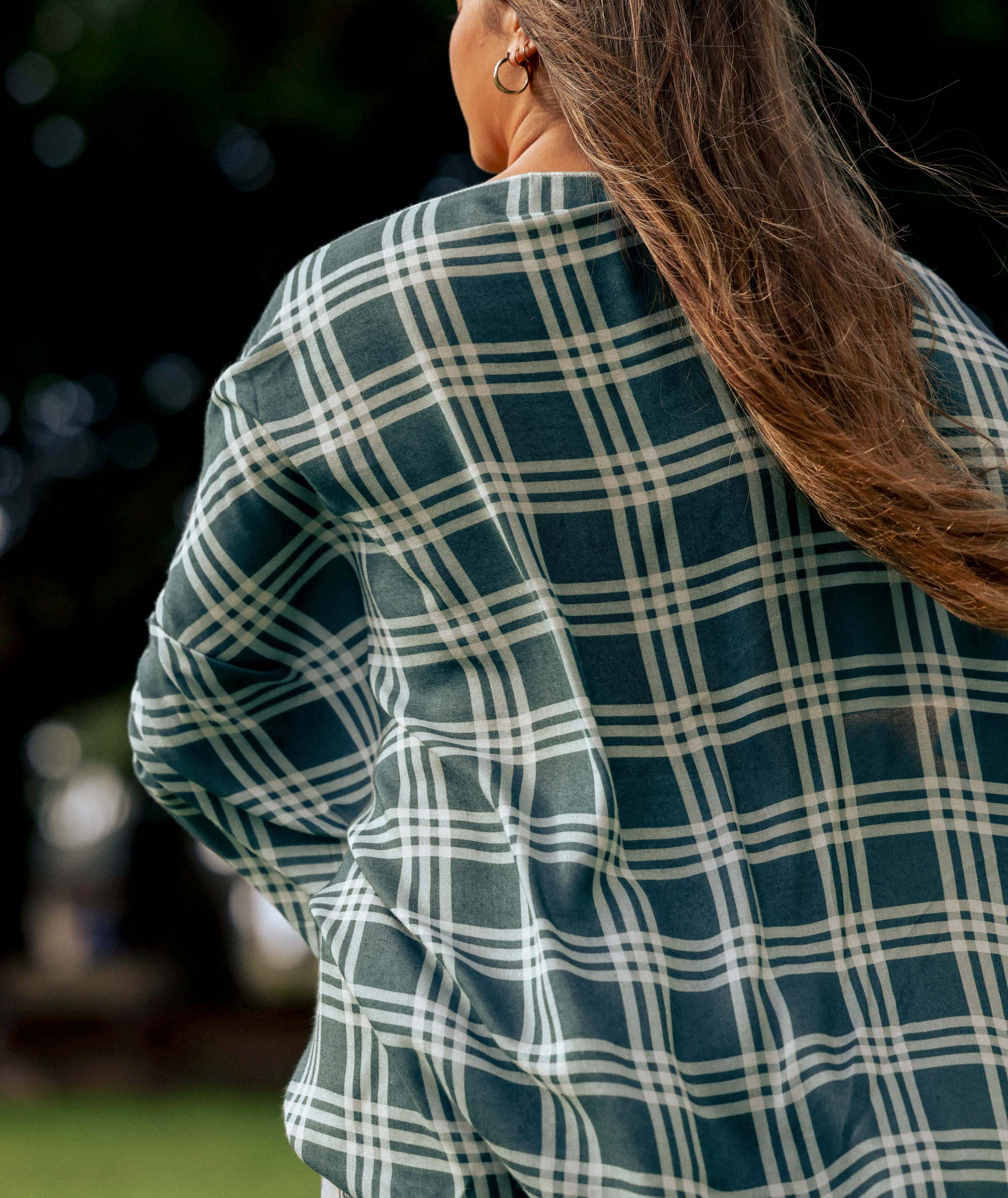Person wearing a green and white plaid shirt with a blurred outdoor background