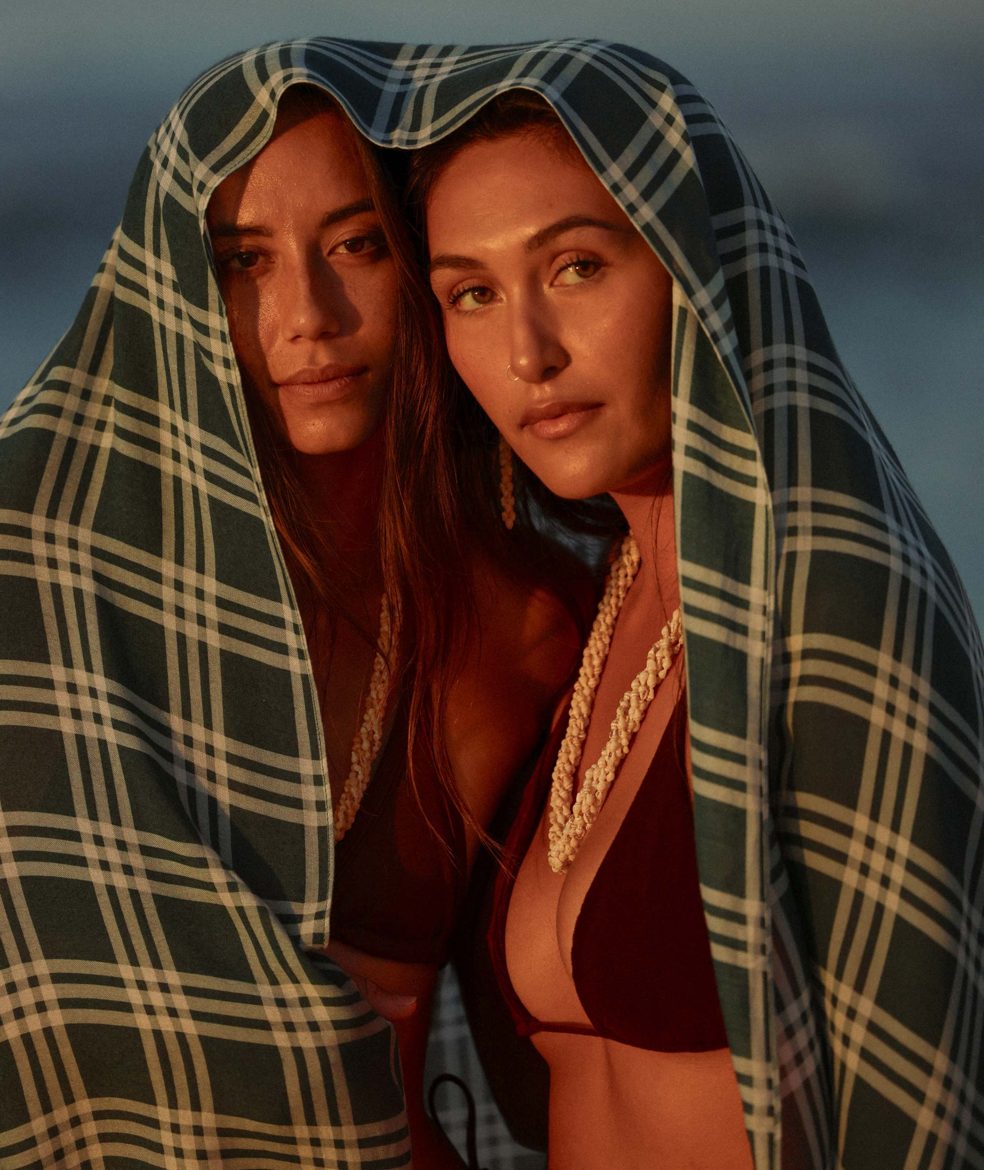 Two women wrapped in a plaid blanket against a dark background