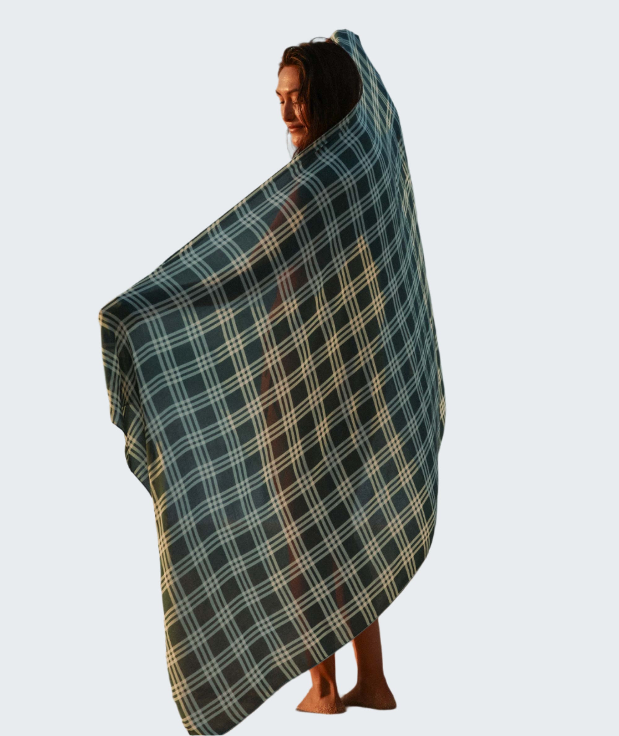 Person wrapped in a plaid blanket on a beach with ocean in the background