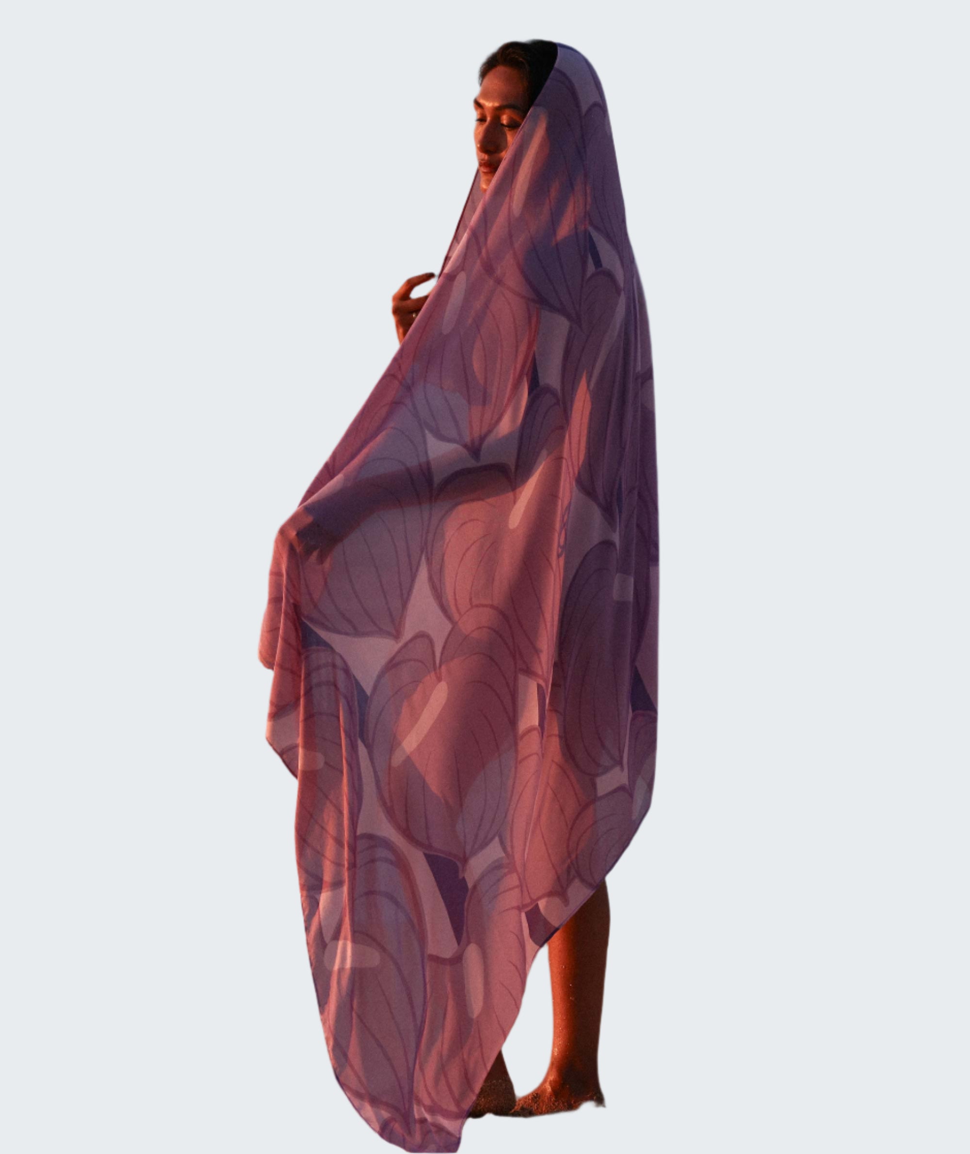 Person wrapped in a purple patterned towel on a beach with ocean waves in the background