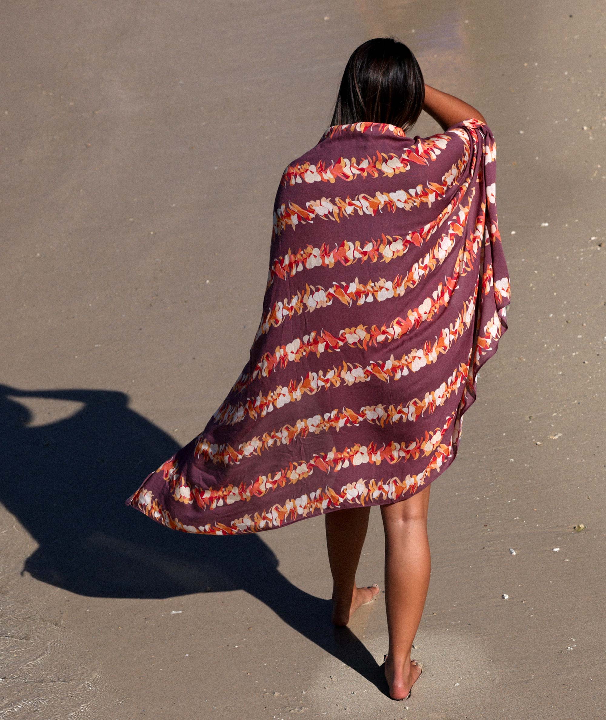Person wrapped in a patterned towel on a sandy beach
