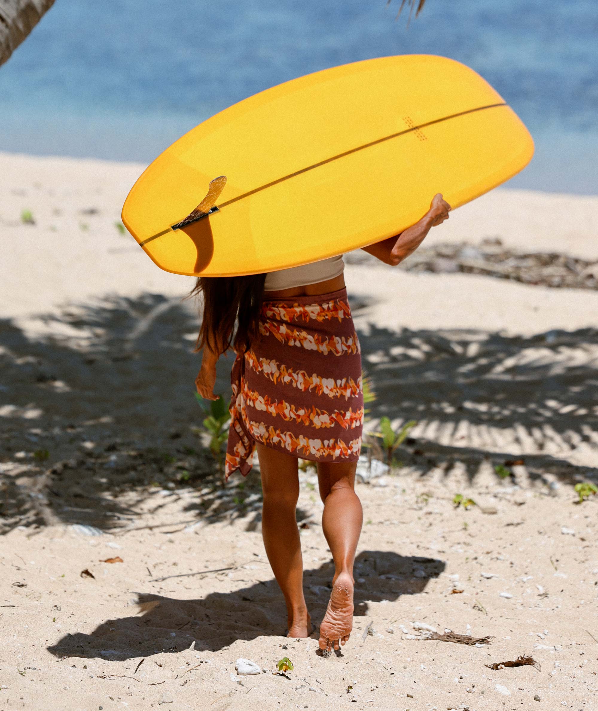 Person holding a yellow surfboard on a sandy beach with ocean in the background