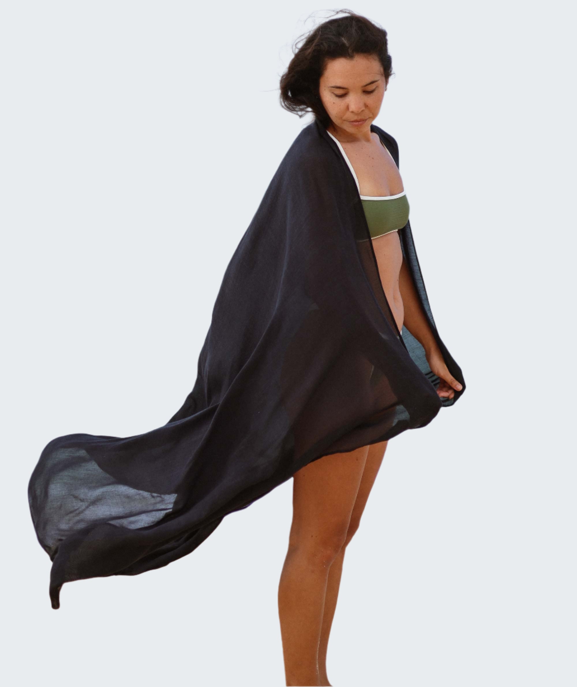 Woman on a beach wearing a black cover-up and green bikini.