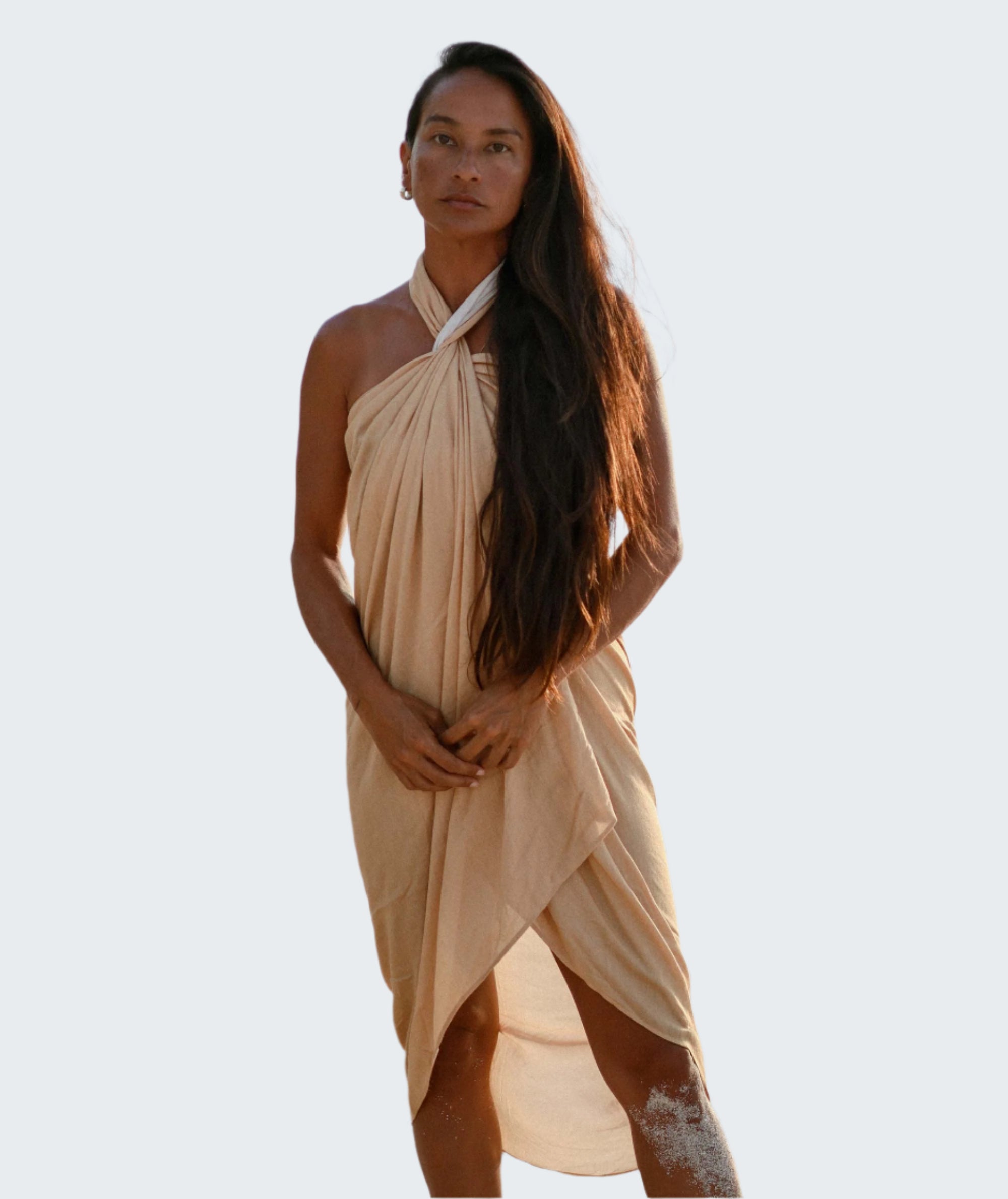 Woman in a beige dress standing on a sandy beach with ocean in the background