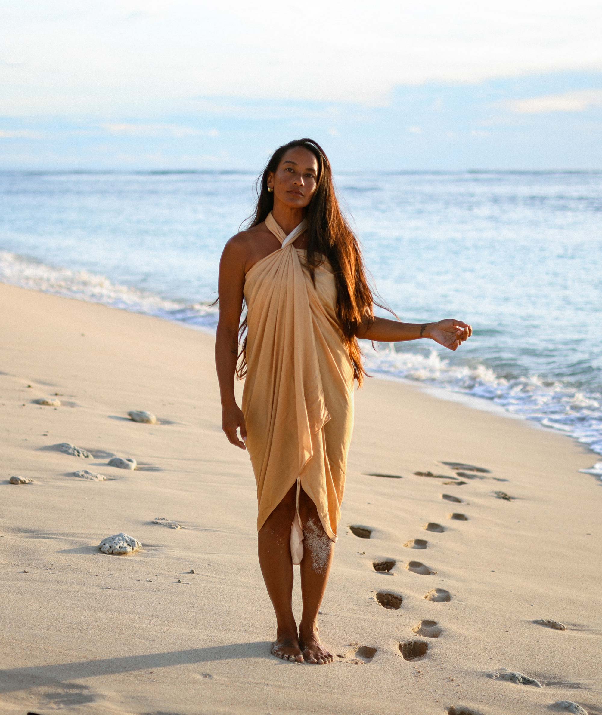 Woman in a beige dress standing on a sandy beach with ocean waves in the background