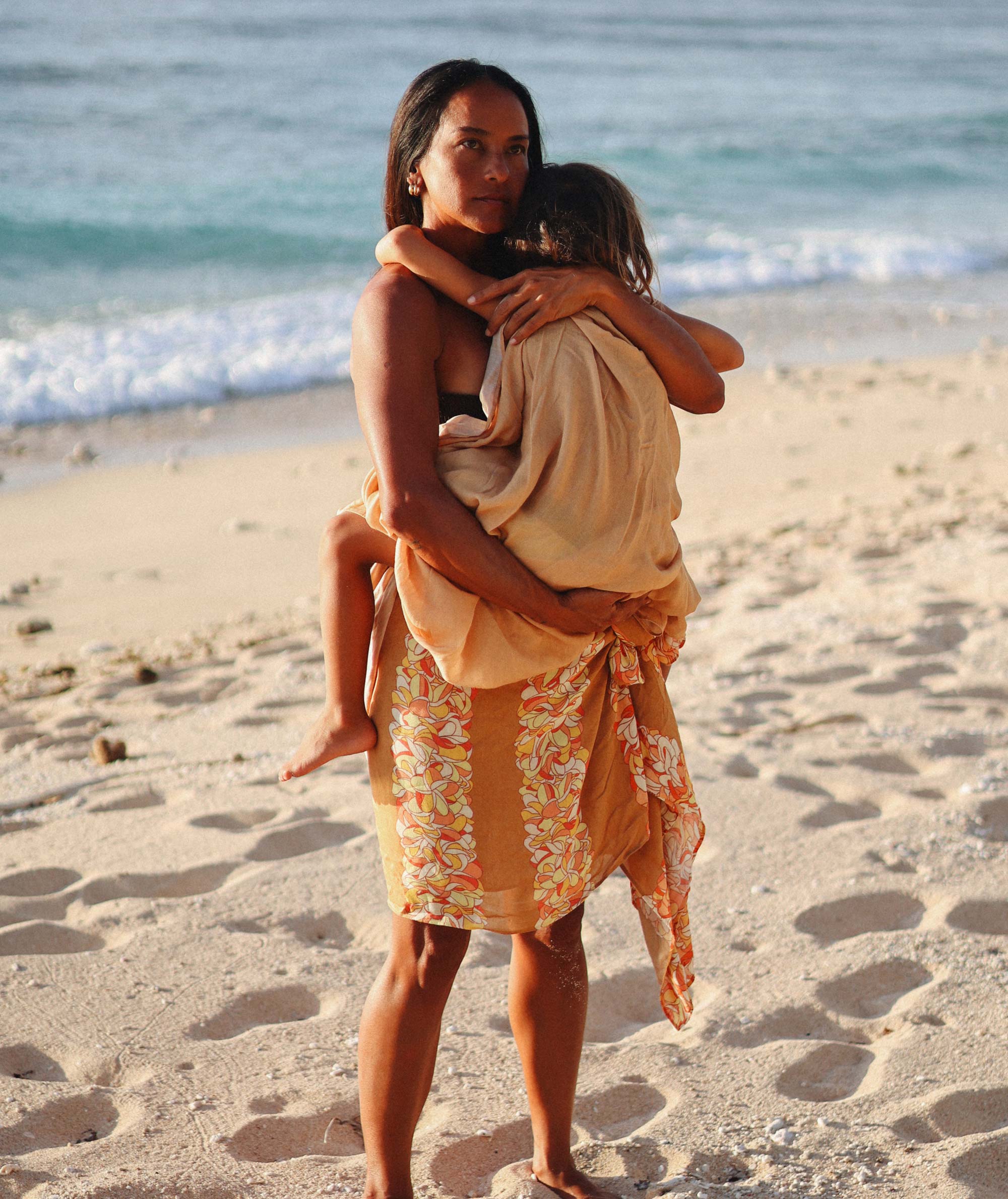 Woman holding a child on a beach with ocean waves in the background