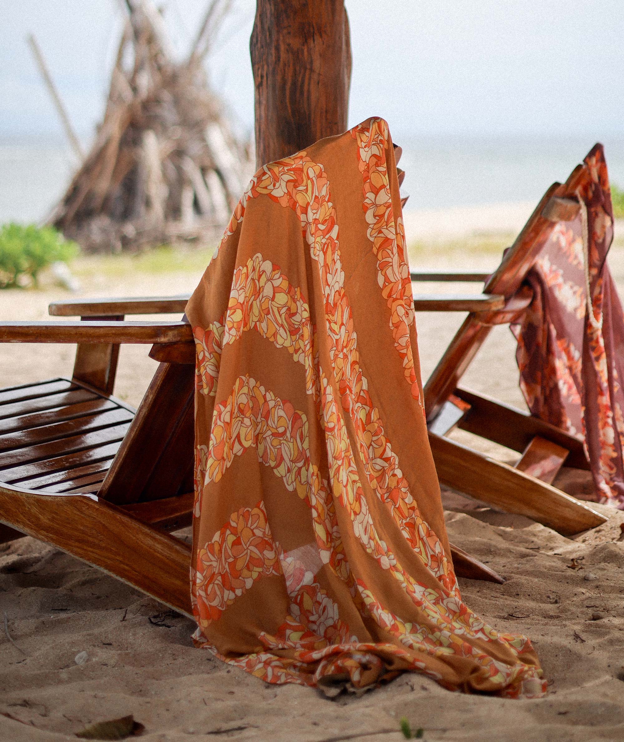 Floral patterned towel draped over a wooden bench on a sandy beach.