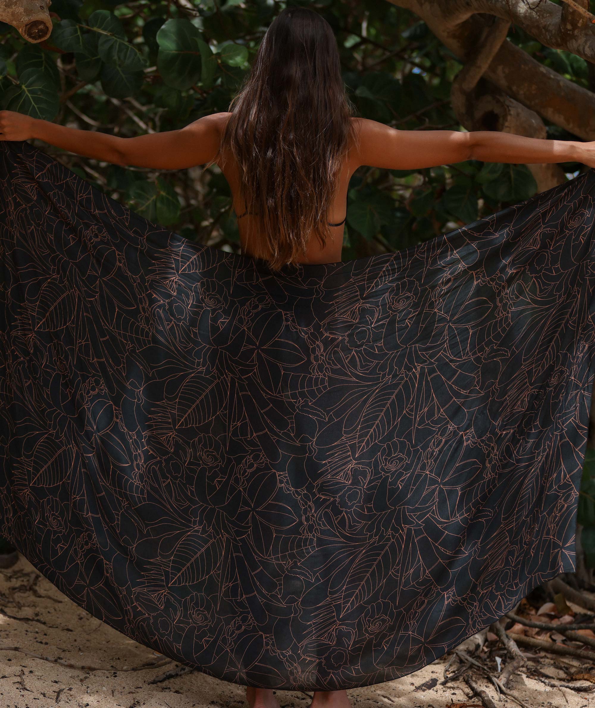 Woman with a dark floral-patterned dress standing outdoors with trees in the background
