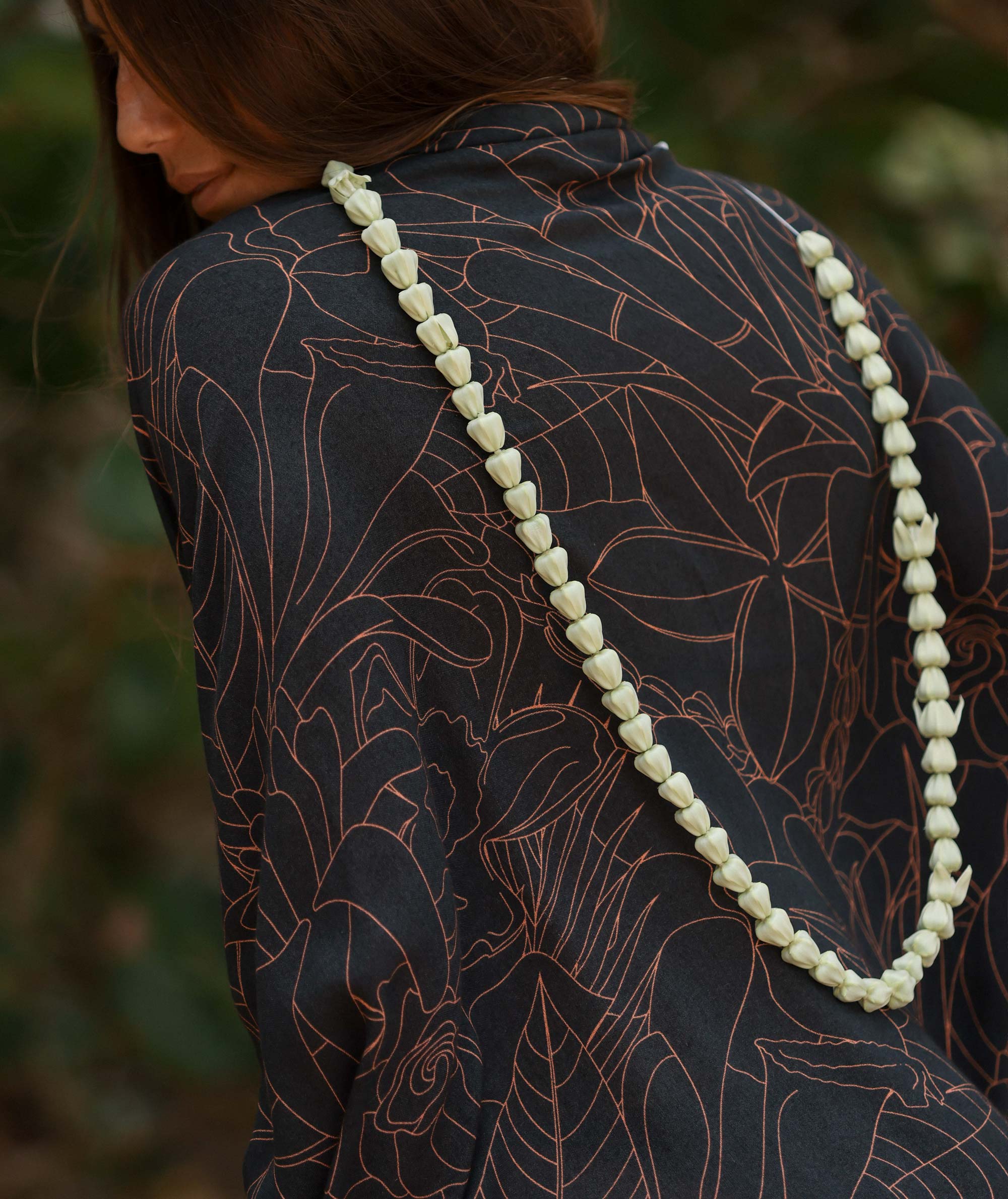 Person wearing a dark patterned garment with a long white beaded necklace.