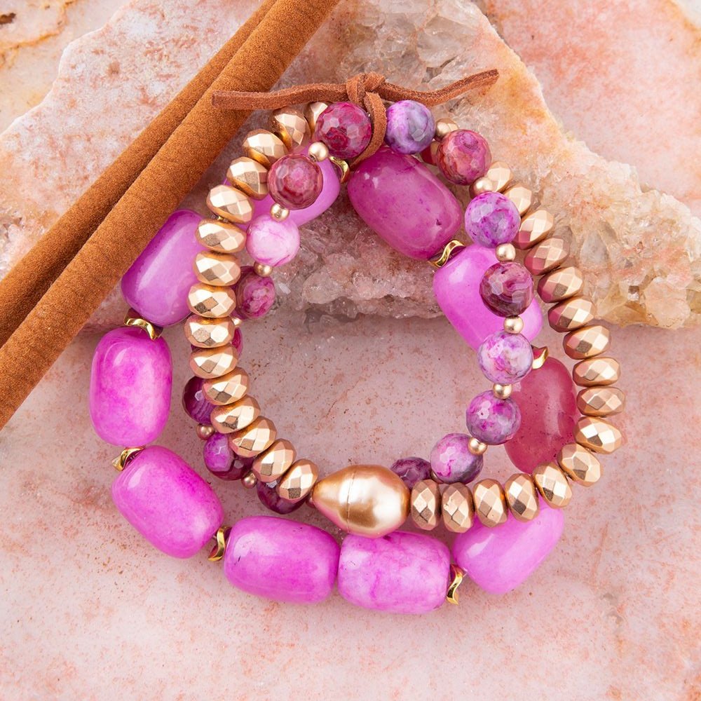 Stack of pink and gold beaded bracelets on a stone surface