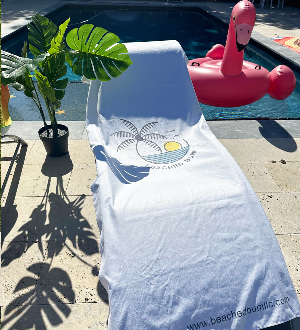 White towel with a logo draped over a lounge chair by a pool, with a pink flamingo floaty in the background.