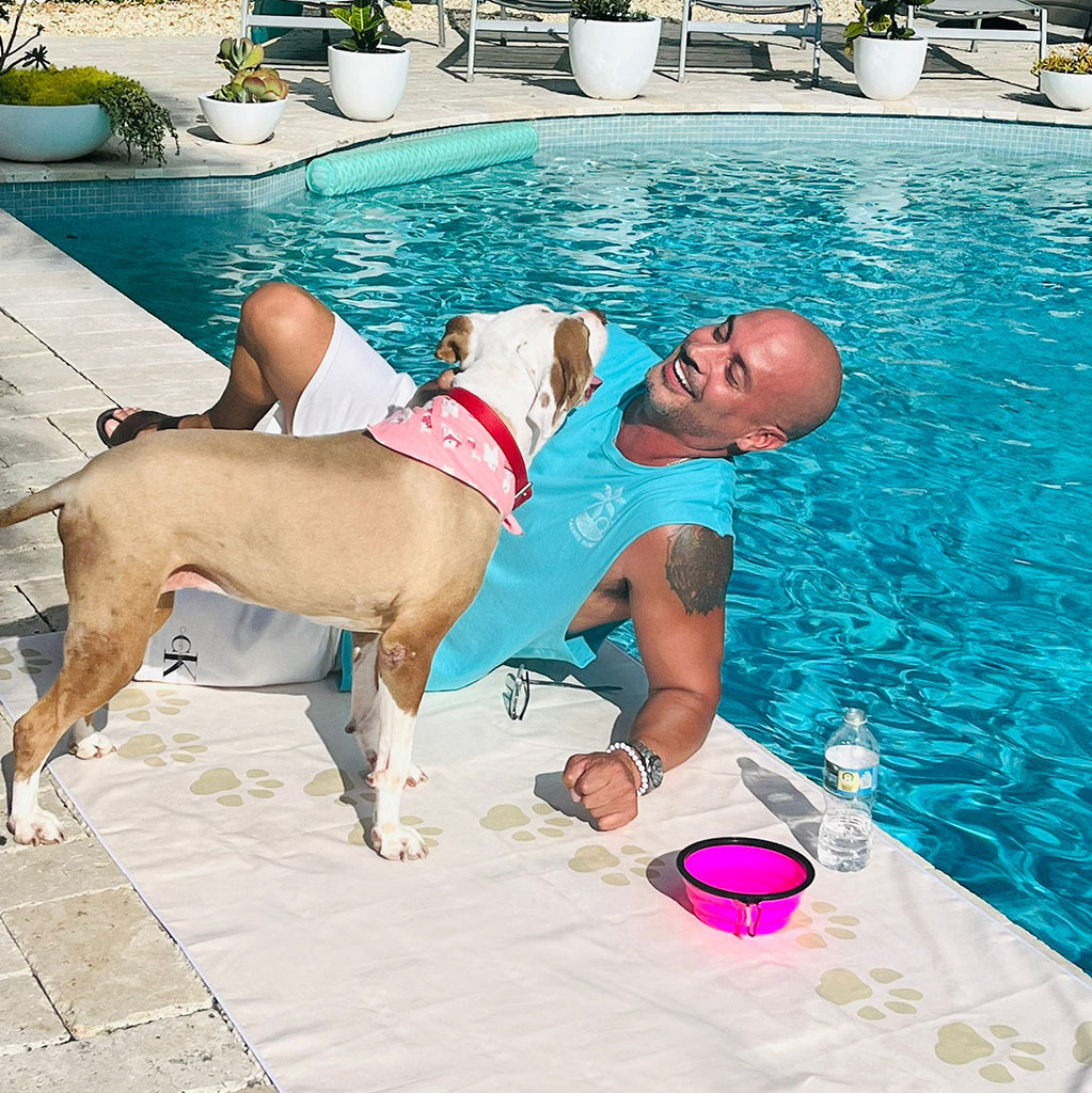 Man and dog by a poolside with a pink bowl and bottle on a towel
