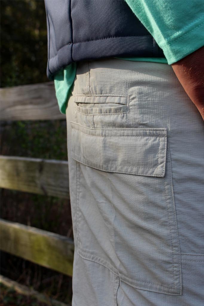 Person wearing light-colored pants with a pocket, standing in front of a wooden fence.