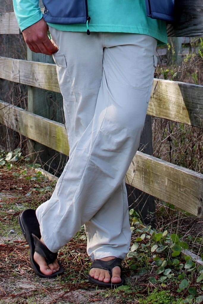 Person wearing light gray pants and sandals standing near a wooden fence.