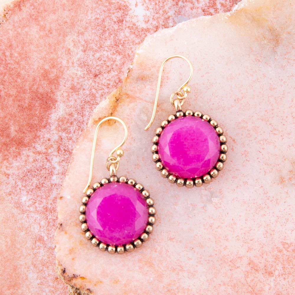 Pink earrings with gold accents on a pink stone background