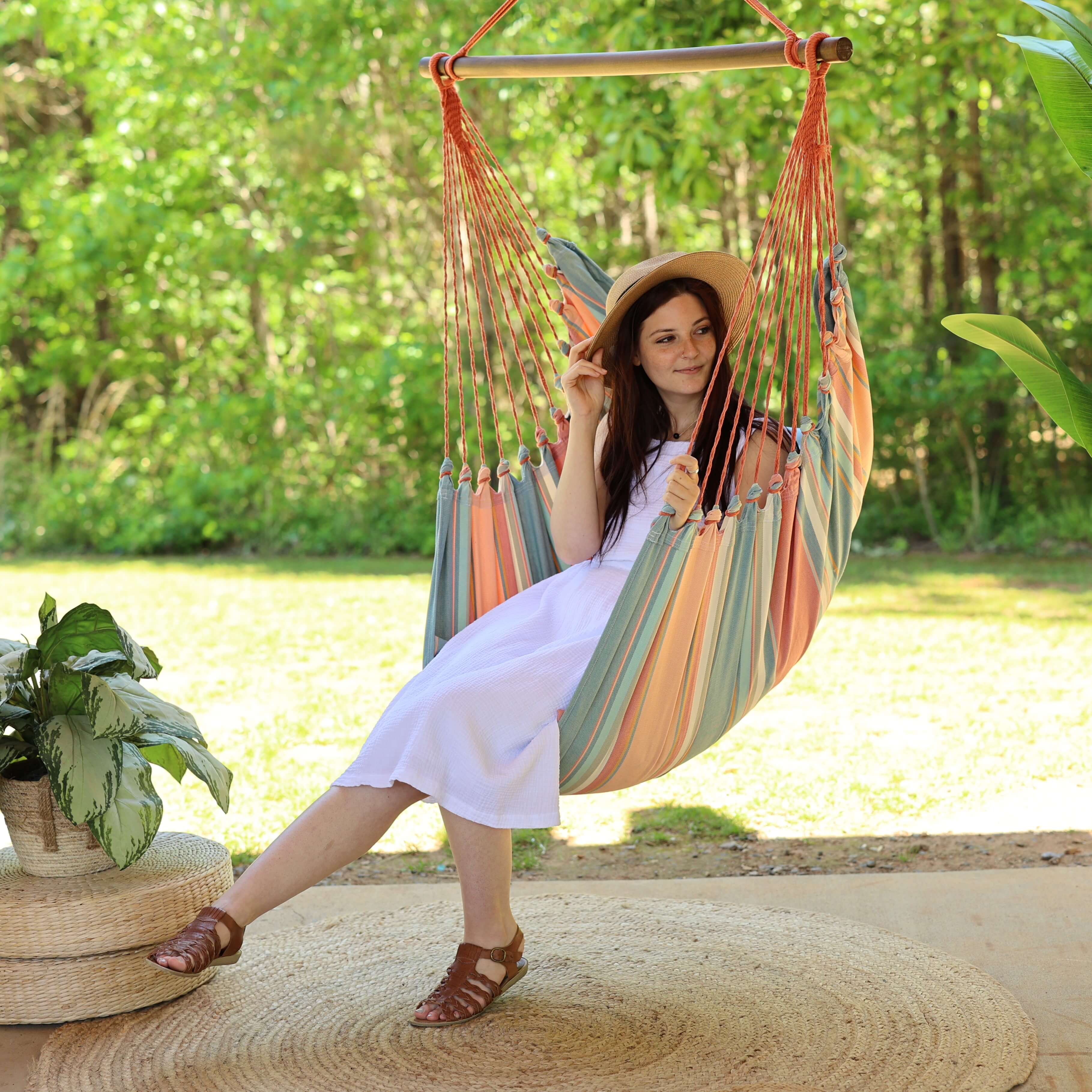 Woman sitting in a colorful hammock chair outdoors with greenery in the background