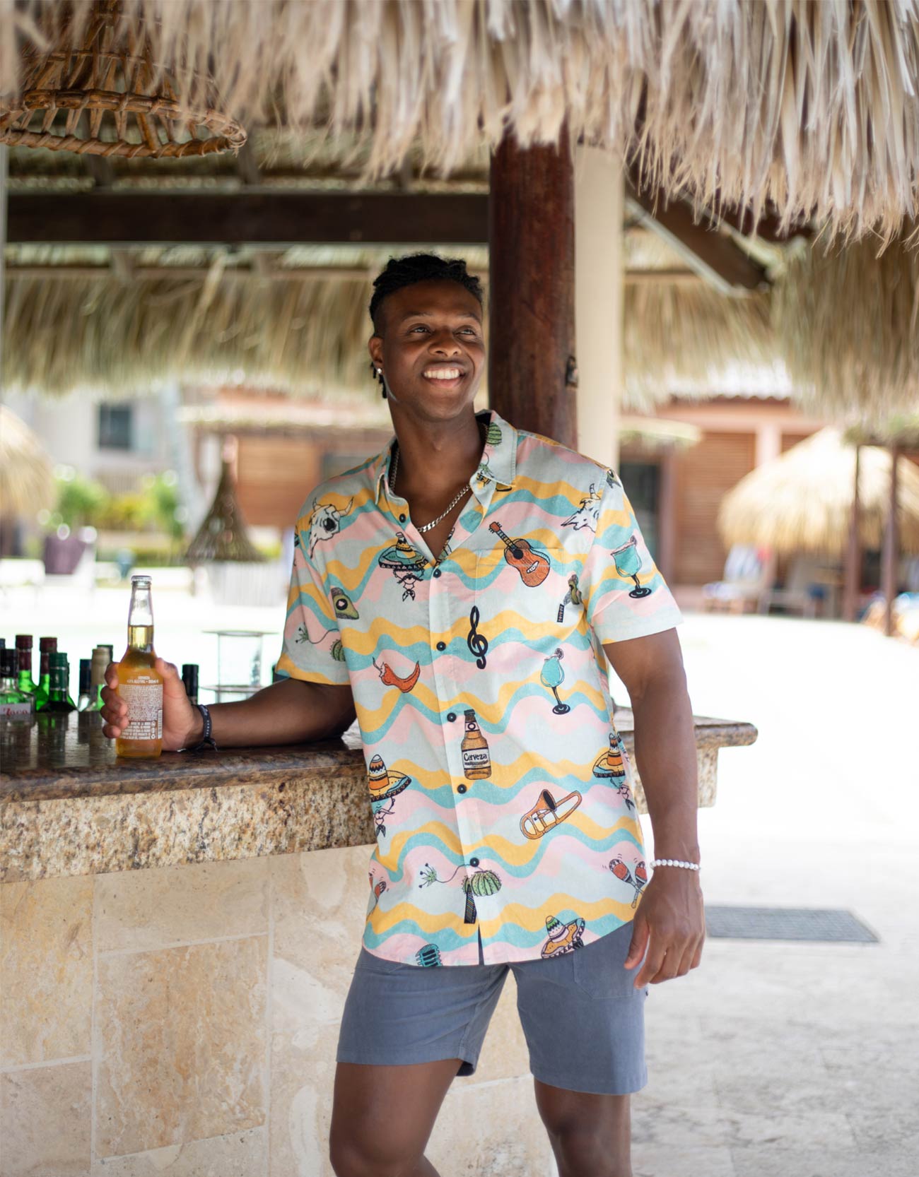 Man in a colorful shirt standing at a bar with a thatched roof