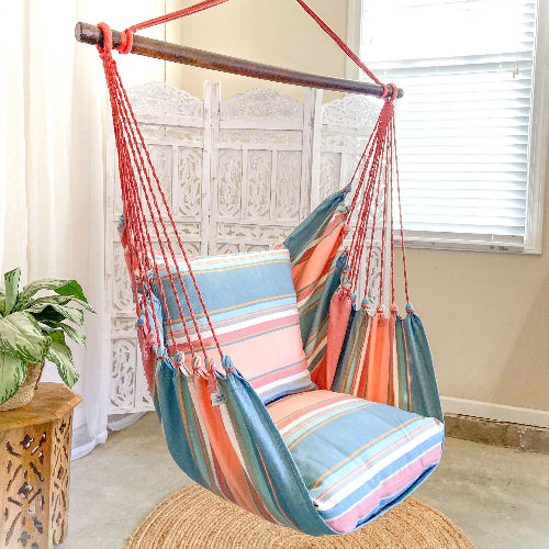 Colorful striped hammock chair in a room with a plant and wooden side table.