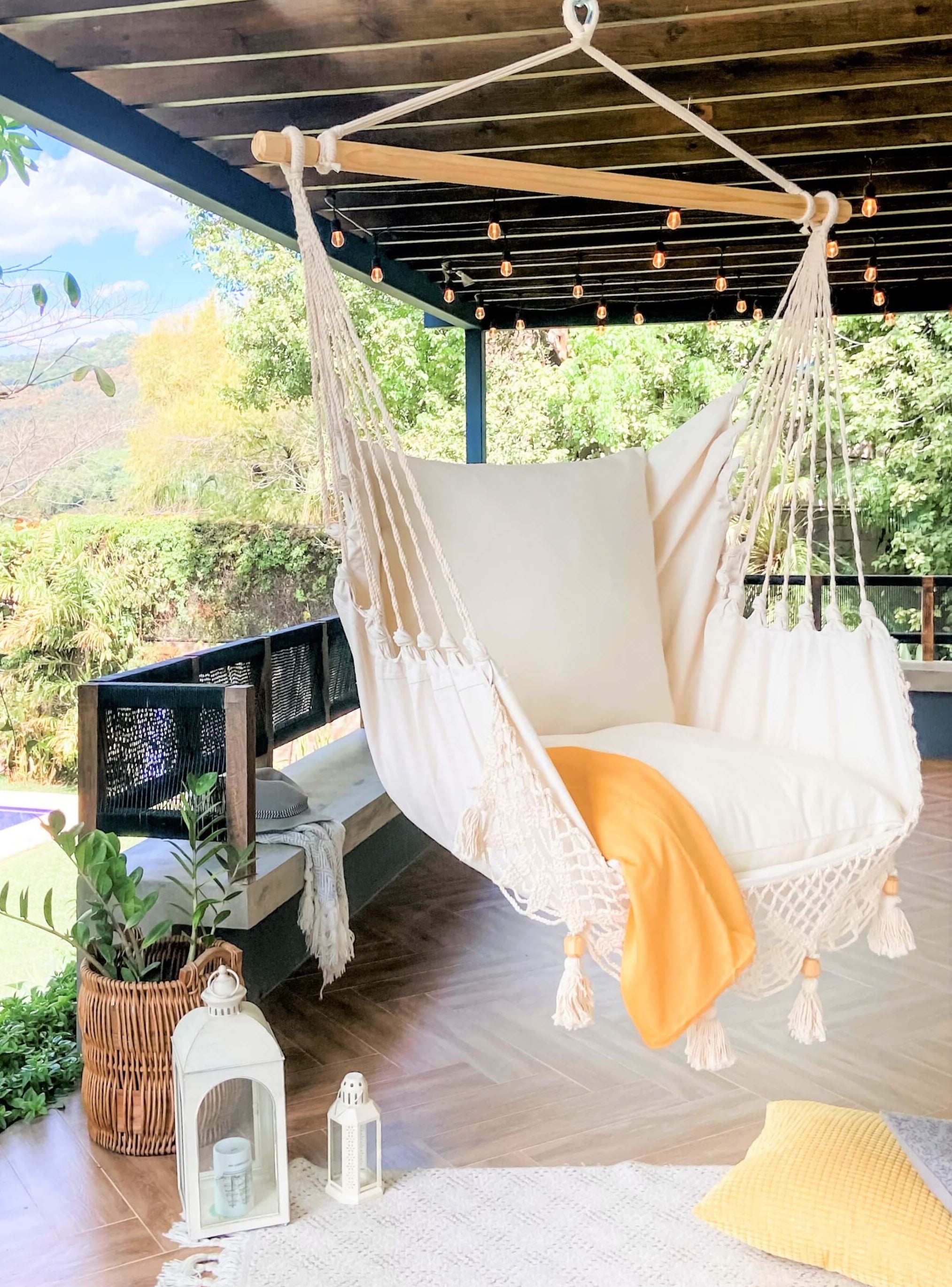 White hammock chair with yellow blanket in a outdoor setting with greenery