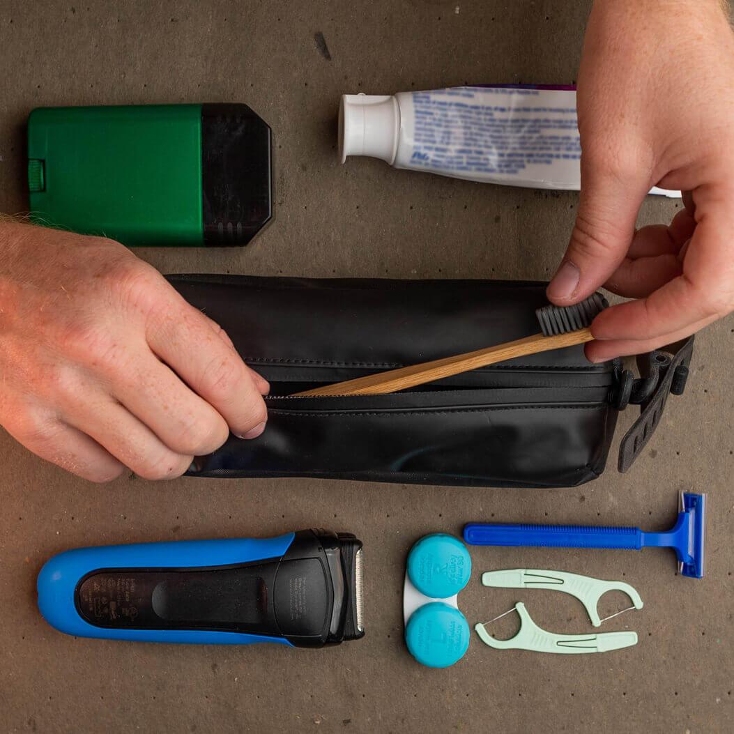 Person organizing grooming tools including a brush, razor, and other items on a brown surface.