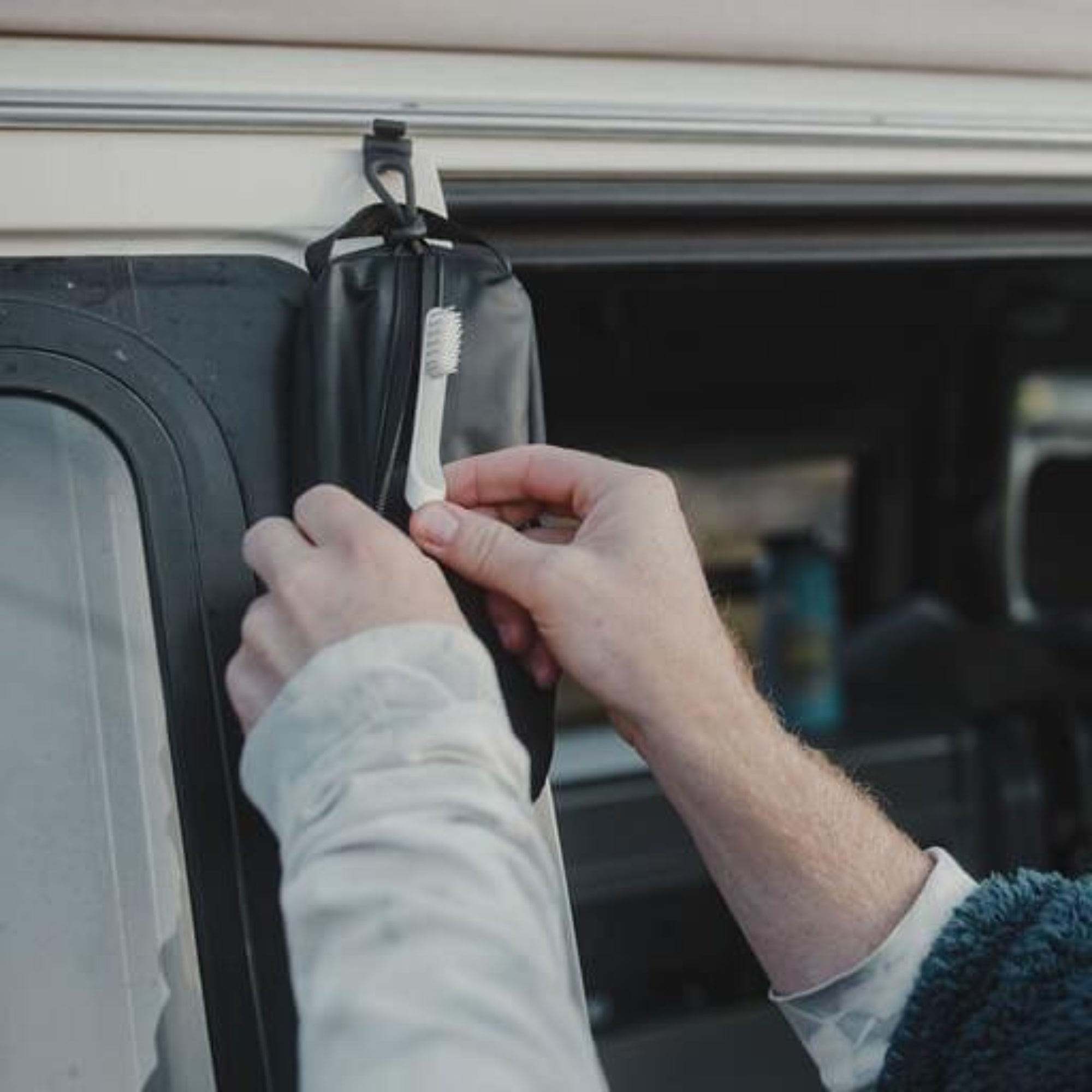 Person hanging a black bag with a white brush on a hook inside a vehicle.