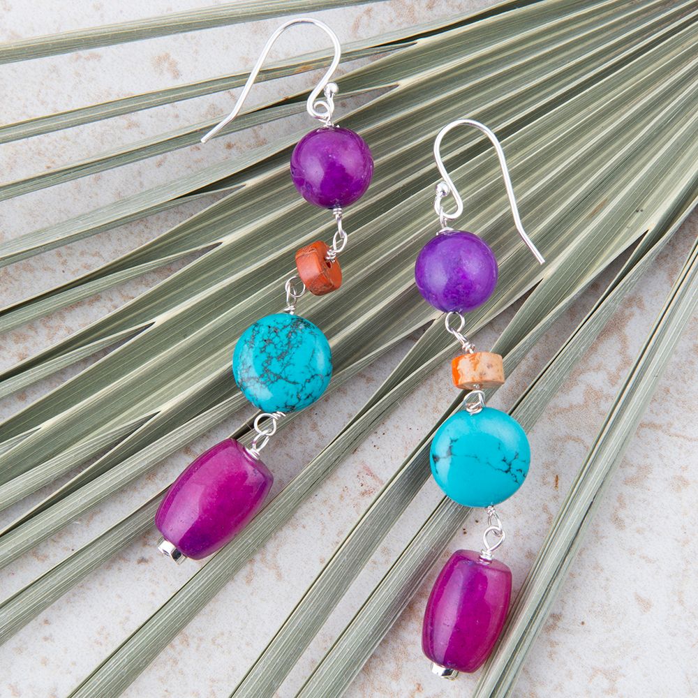 Pair of earrings with purple and turquoise beads on a leafy background