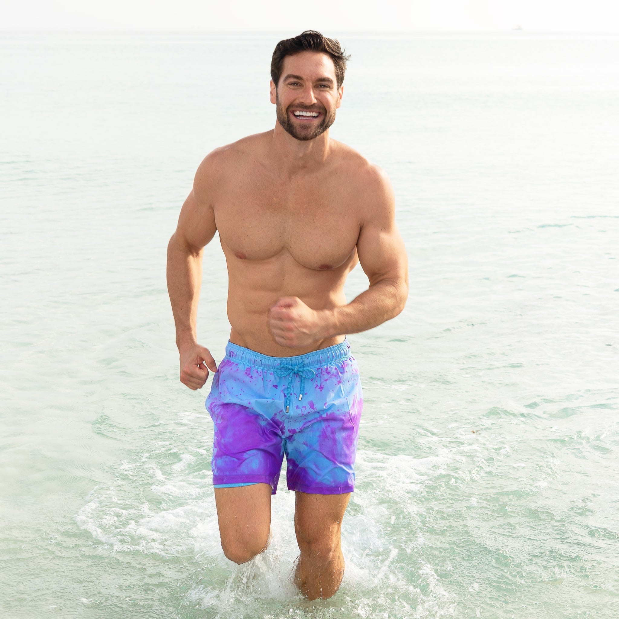 Man wearing colorful swim shorts running through shallow water.