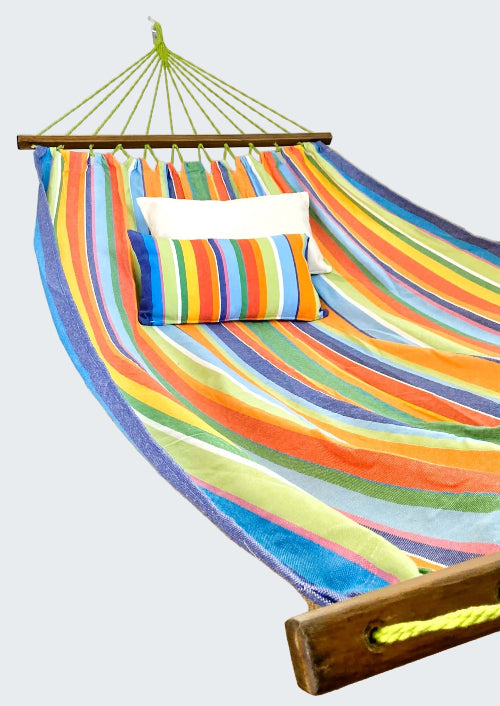Colorful striped hammock with pillows on a wooden stand against a white curtain background.
