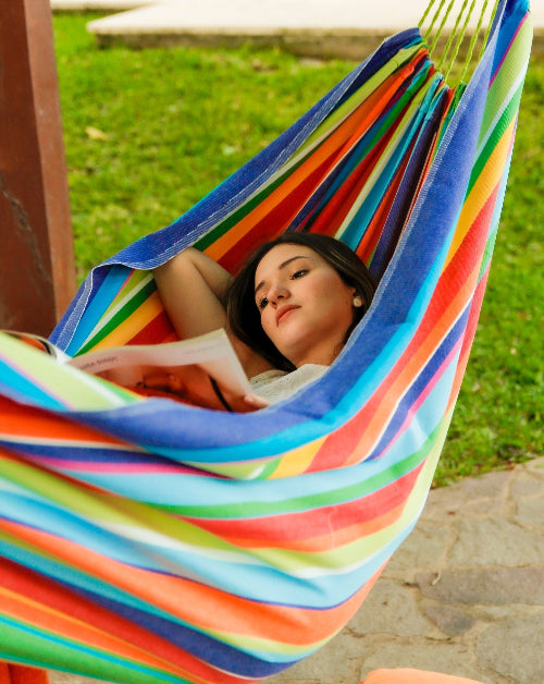 Woman relaxing in a colorful striped hammock outdoors.