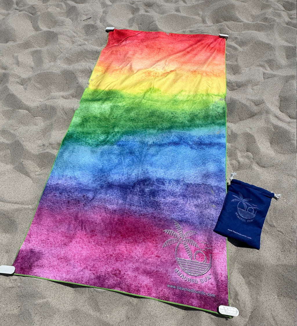 Rainbow gradient towel on sand with a blue pouch