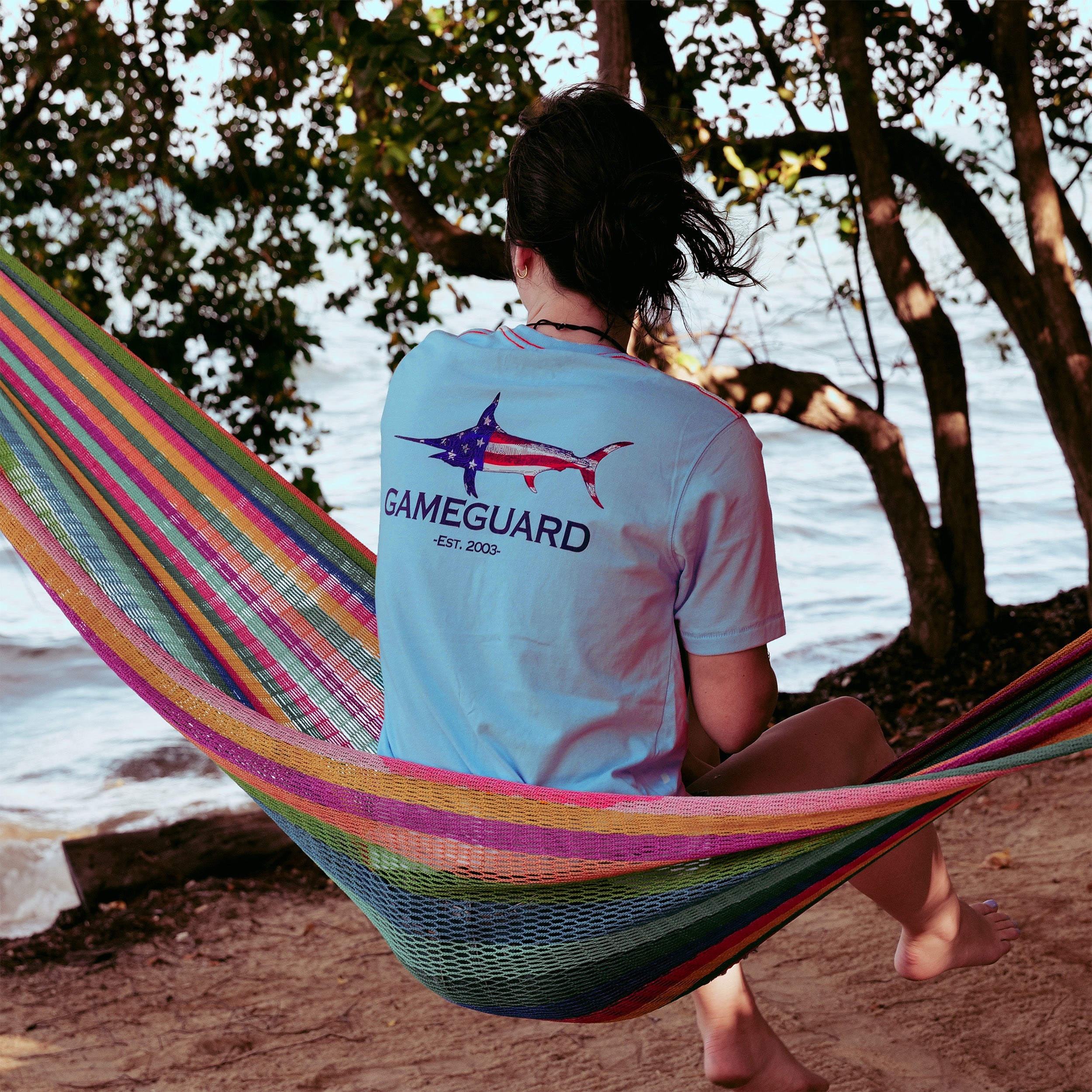 Person sitting in a colorful hammock by the beach wearing a GameGuard shirt.