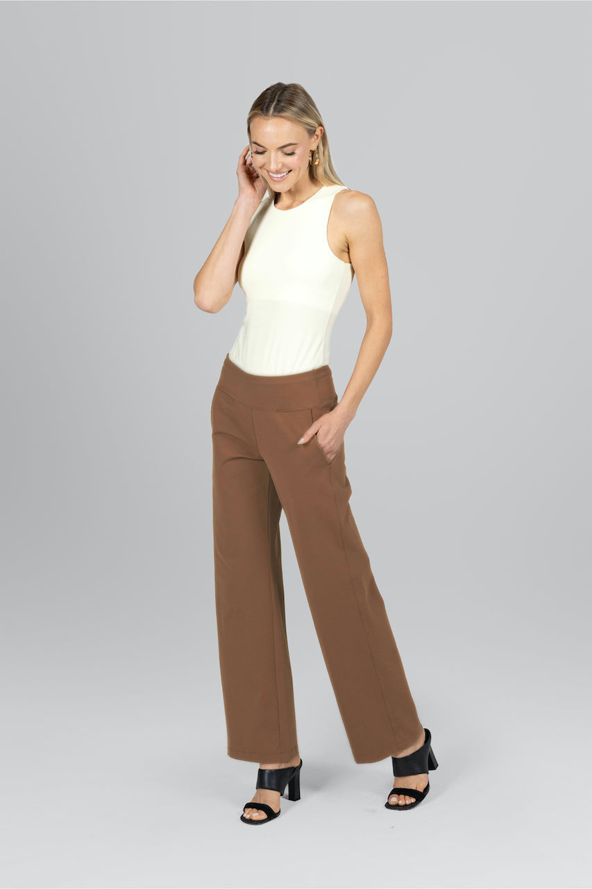 Woman wearing a white sleeveless top and brown high-waisted pants on a gray background