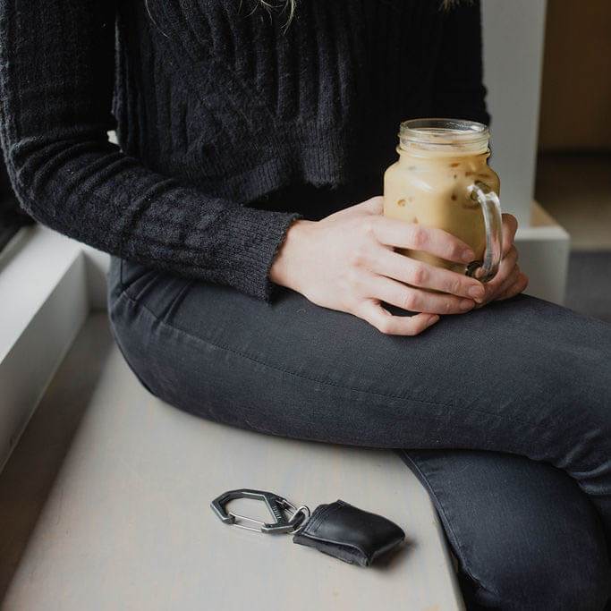 Person holding a mason jar with iced coffee on a windowsill.