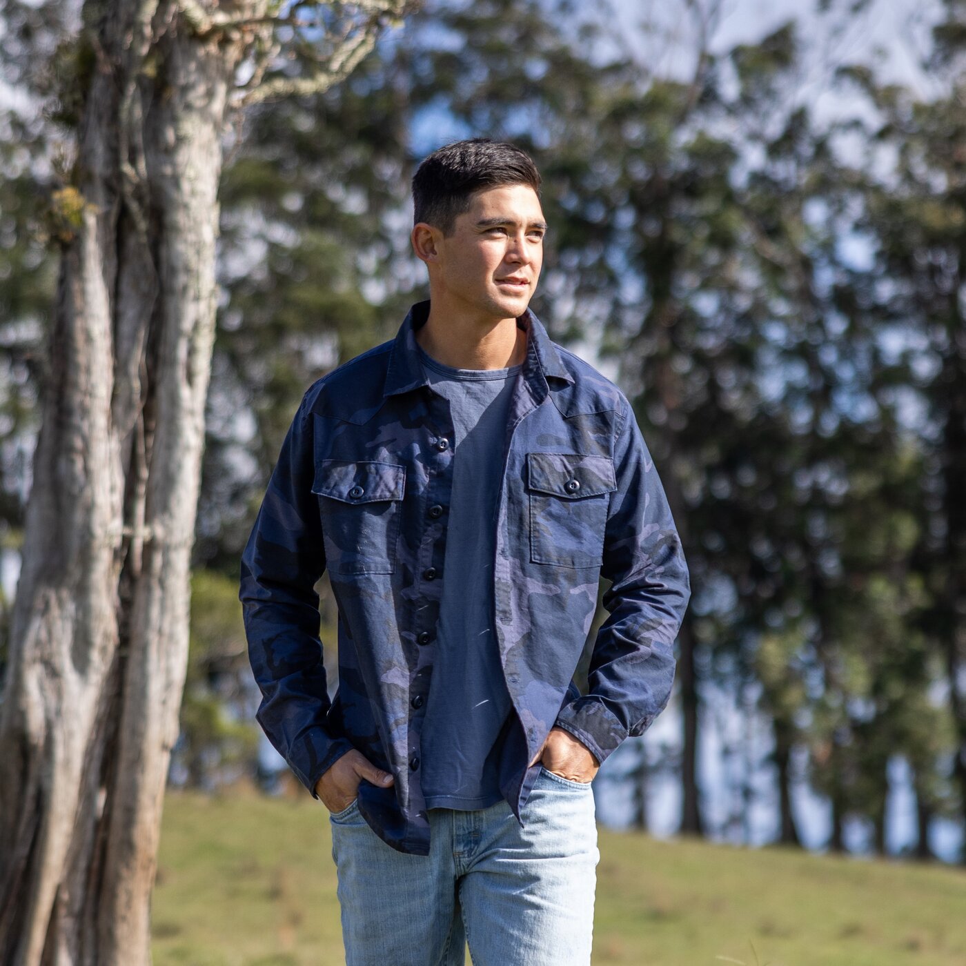 Man wearing a blue denim jacket standing outdoors with trees in the background