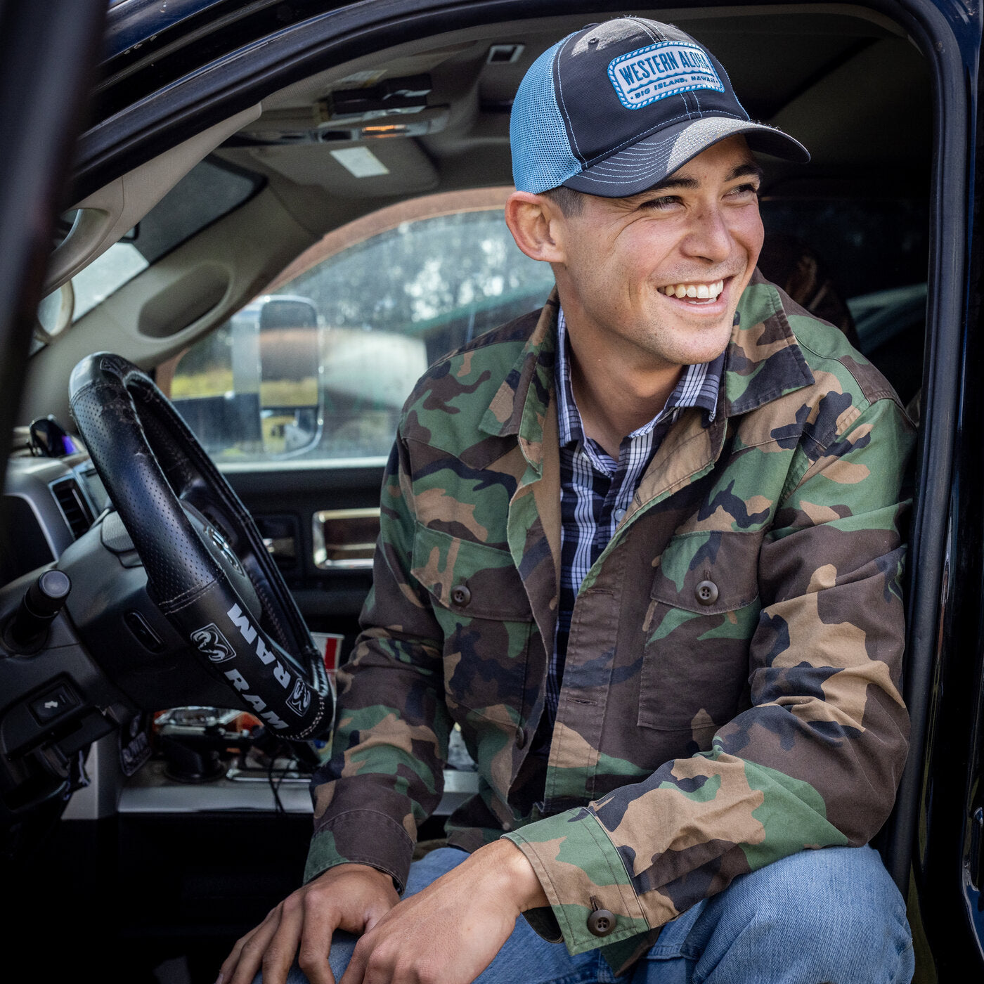 Man wearing a camouflage jacket and cap sitting inside a vehicle
