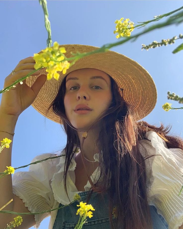 Woman wearing a straw hat and overalls with yellow flowers against a blue sky.