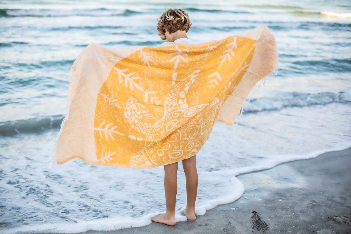 Person standing on a beach with a yellow and white patterned towel draped over them