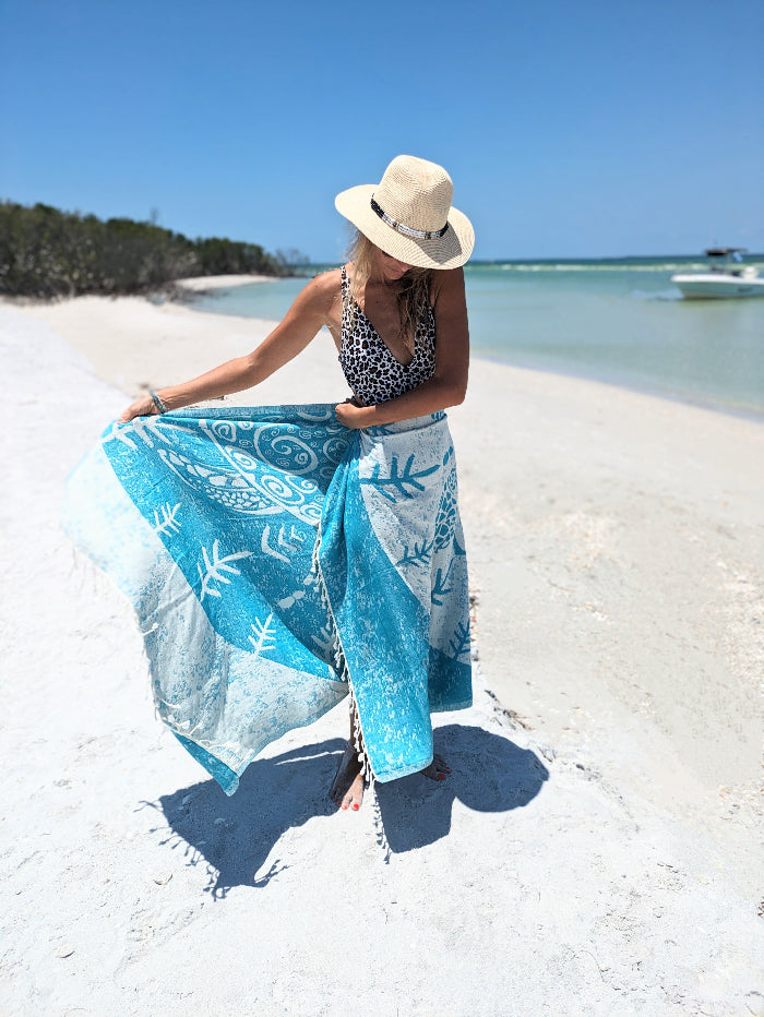 Woman on a beach holding a blue towel with white patterns