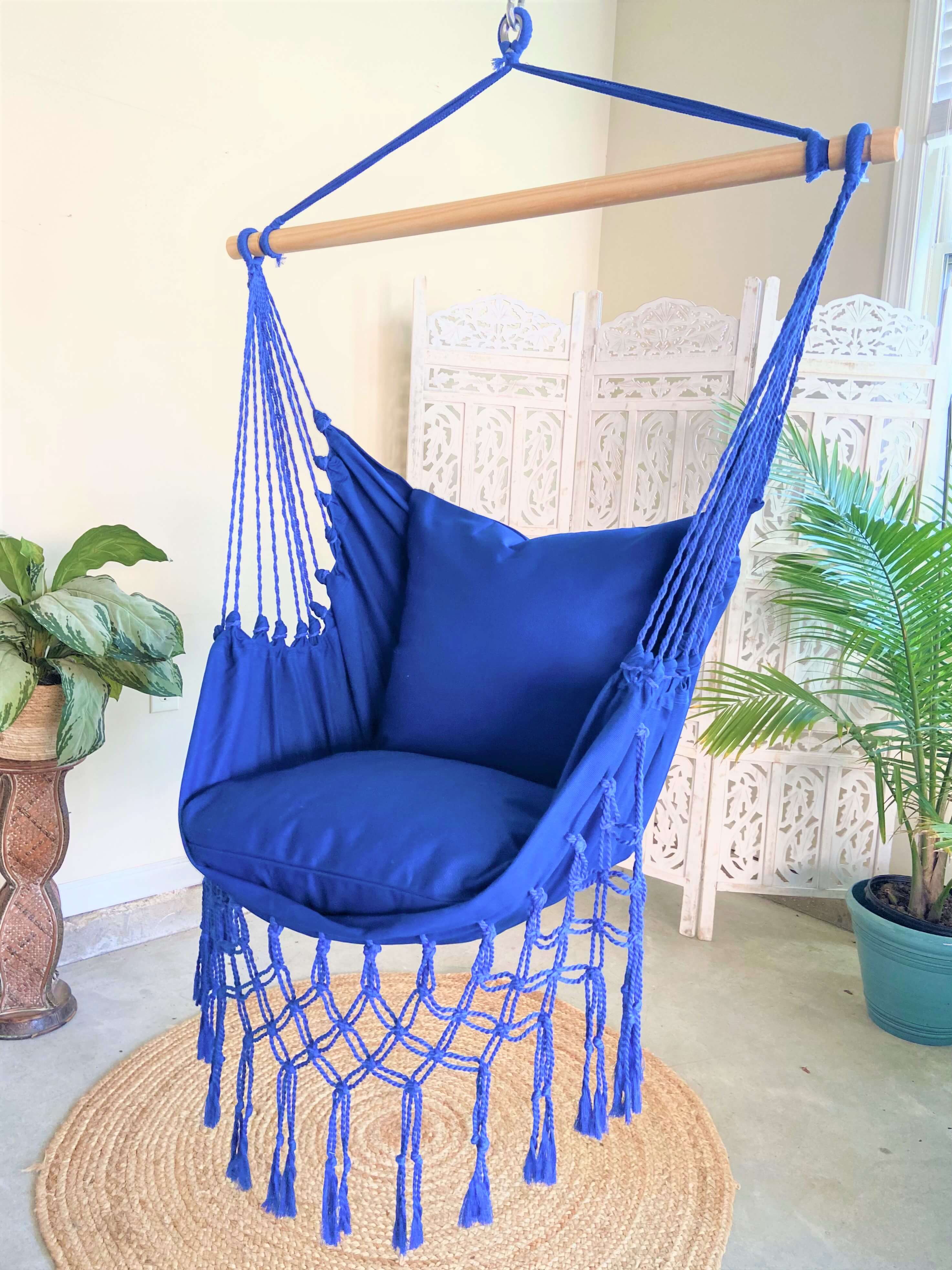 Blue hammock chair with tassels hanging indoors with plants and a white lattice in the background.