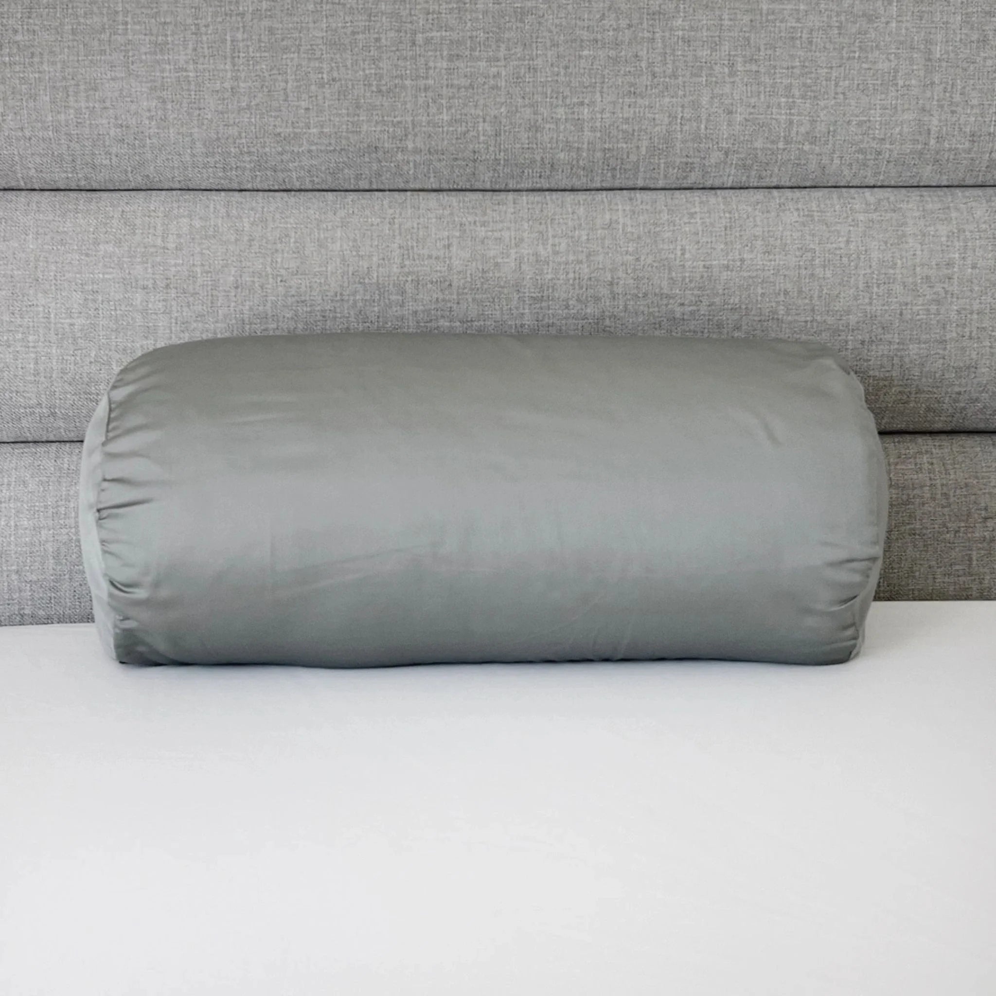 Gray cylindrical pillow on a bed with a gray headboard