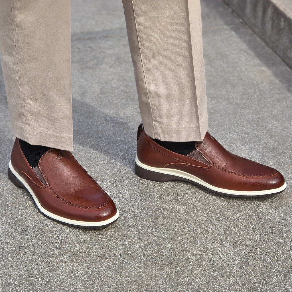 Brown leather shoes worn with beige pants on a gray pavement.