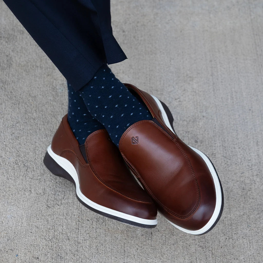 Brown loafers with white soles worn with navy socks on a gray surface