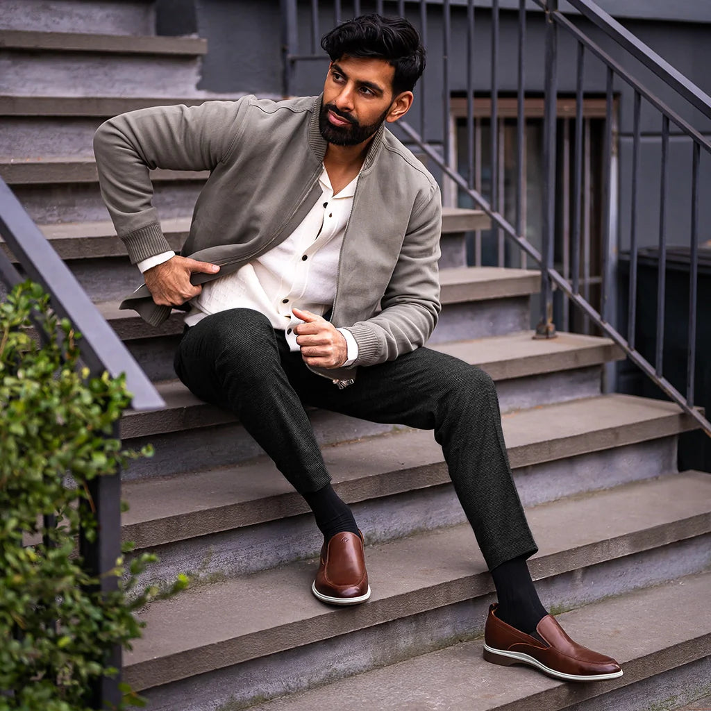 Man sitting on stairs wearing a gray blazer, white shirt, black pants, and brown shoes.