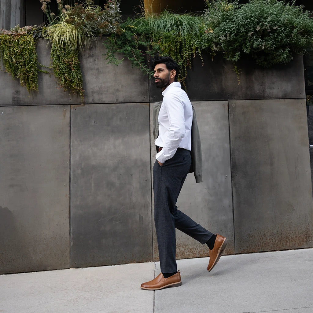 Man in a white shirt and dark pants walking past a concrete wall with plants.