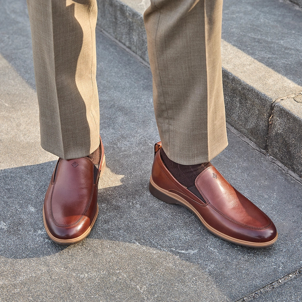 Brown leather shoes worn with beige pants on a concrete surface