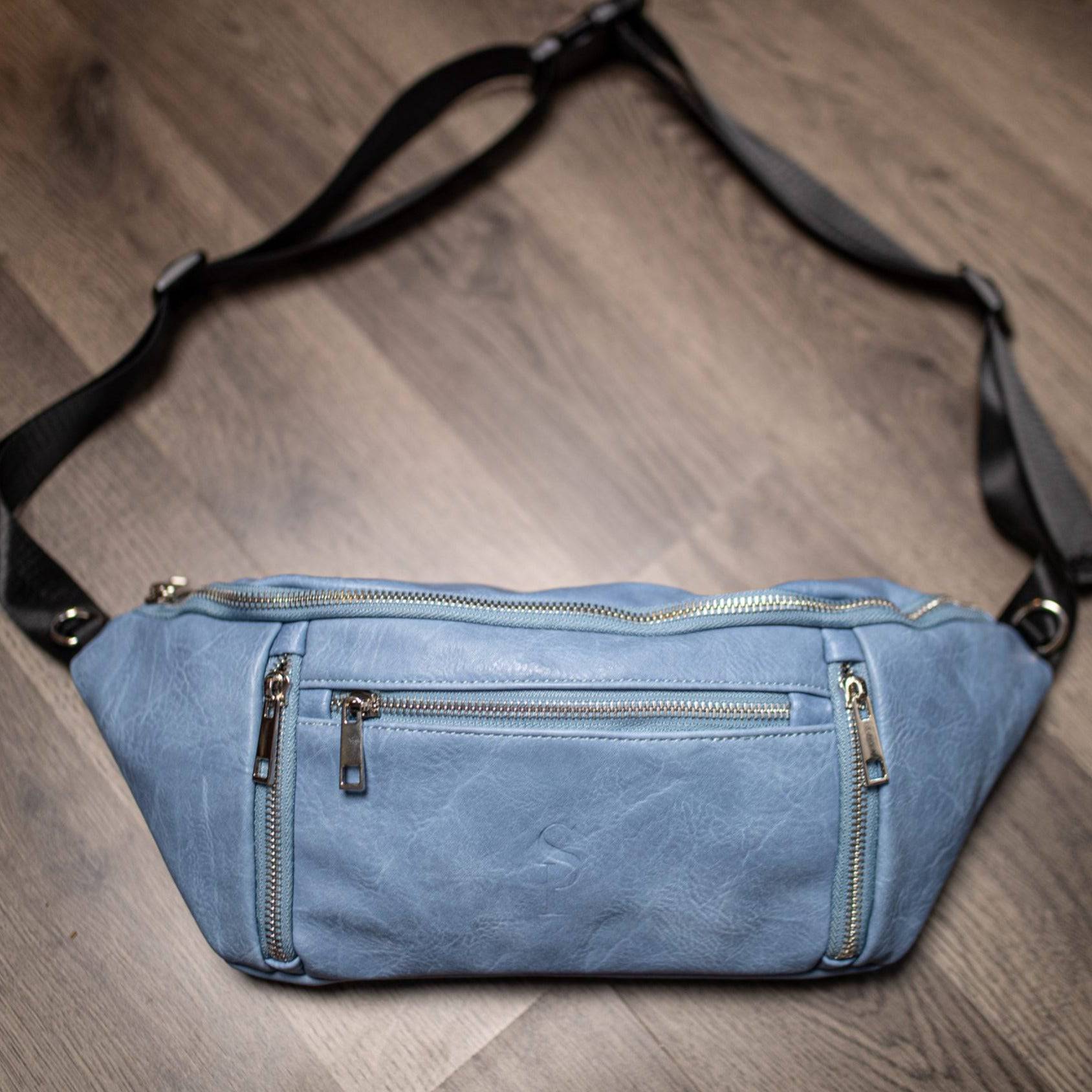 Blue waist bag with zippers on a wooden floor