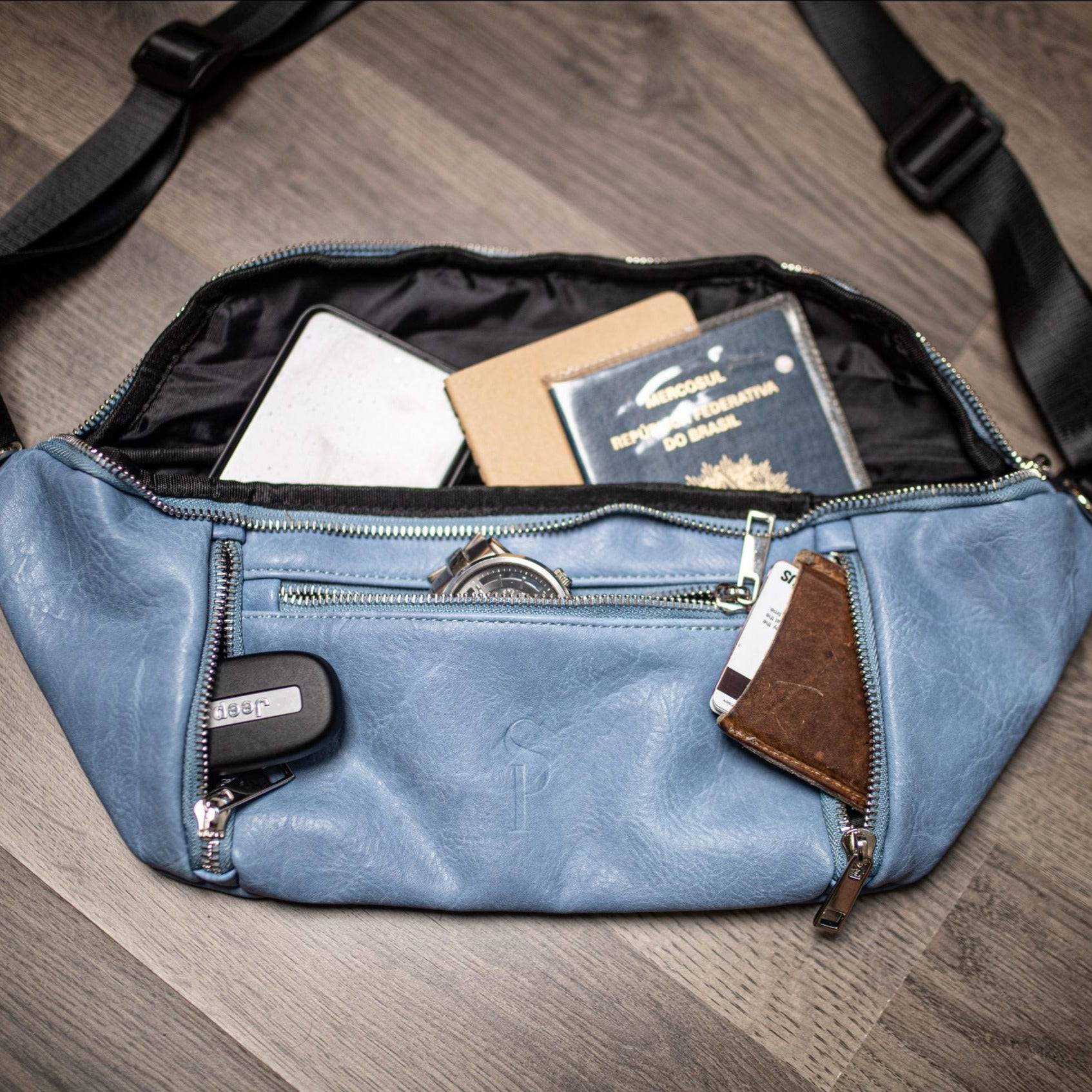 Blue waist bag with items like a passport and wallet on a wooden surface