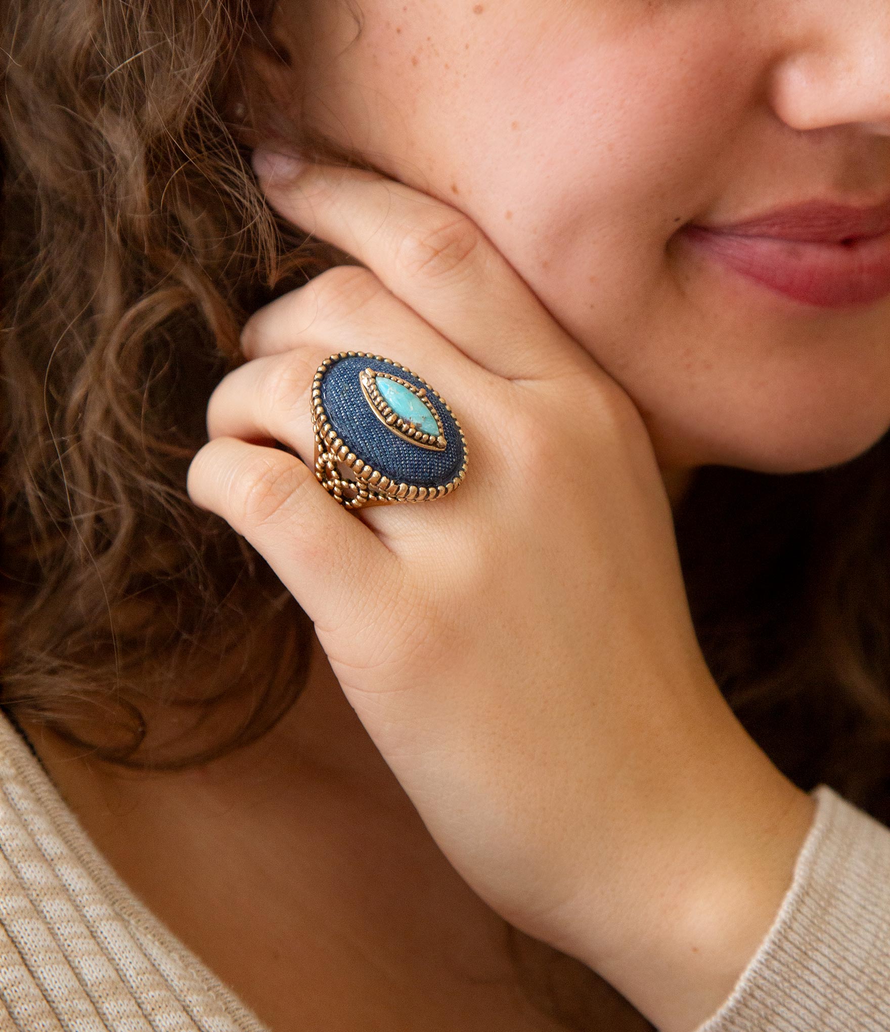Close-up of a person wearing a large, decorative ring with a blue stone.